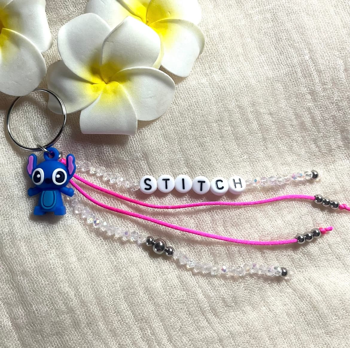 Porte-clé STITCH existe bleu électrique ou fuchsia avec des perles irisées de 3 mm, agrément é de pendentifs blancs avec l'inscription stitch noires et de perles en acier inoxydable. Fabrication Française, atelier situé à Aix en Provence