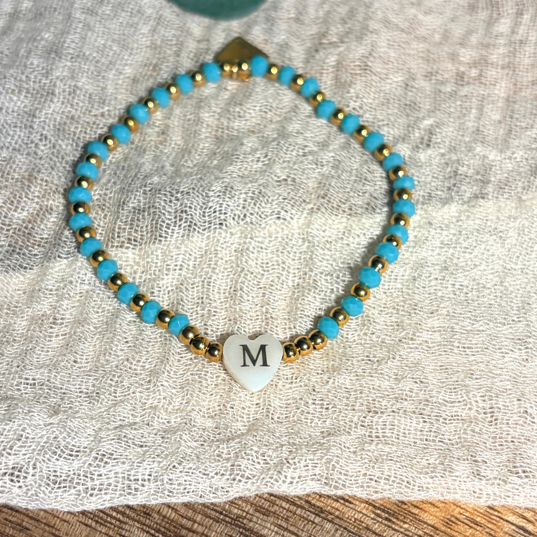 Bracelet femme en perles à facettes de différents coloris, rouge, beige, corail, marine et turquoise, de perles dorées en acier inoxydable et d'un pendentif cœur en véritable nacre de coquillage orné d'une initiale conçu sur mesure avec des perles de trois millimètres fabriquée à la main à Aix-en-Provence