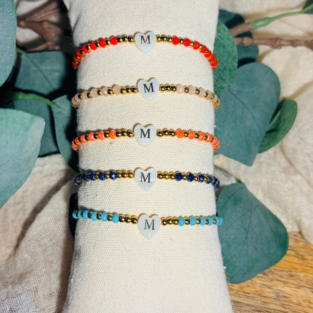 Bracelet femme en perles à facettes de différents coloris, rouge, beige, corail, marine et turquoise, de perles dorées en acier inoxydable et d'un pendentif cœur en véritable nacre de coquillage orné d'une initiale conçu sur mesure avec des perles de trois millimètres fabriquée à la main à Aix-en-Provence