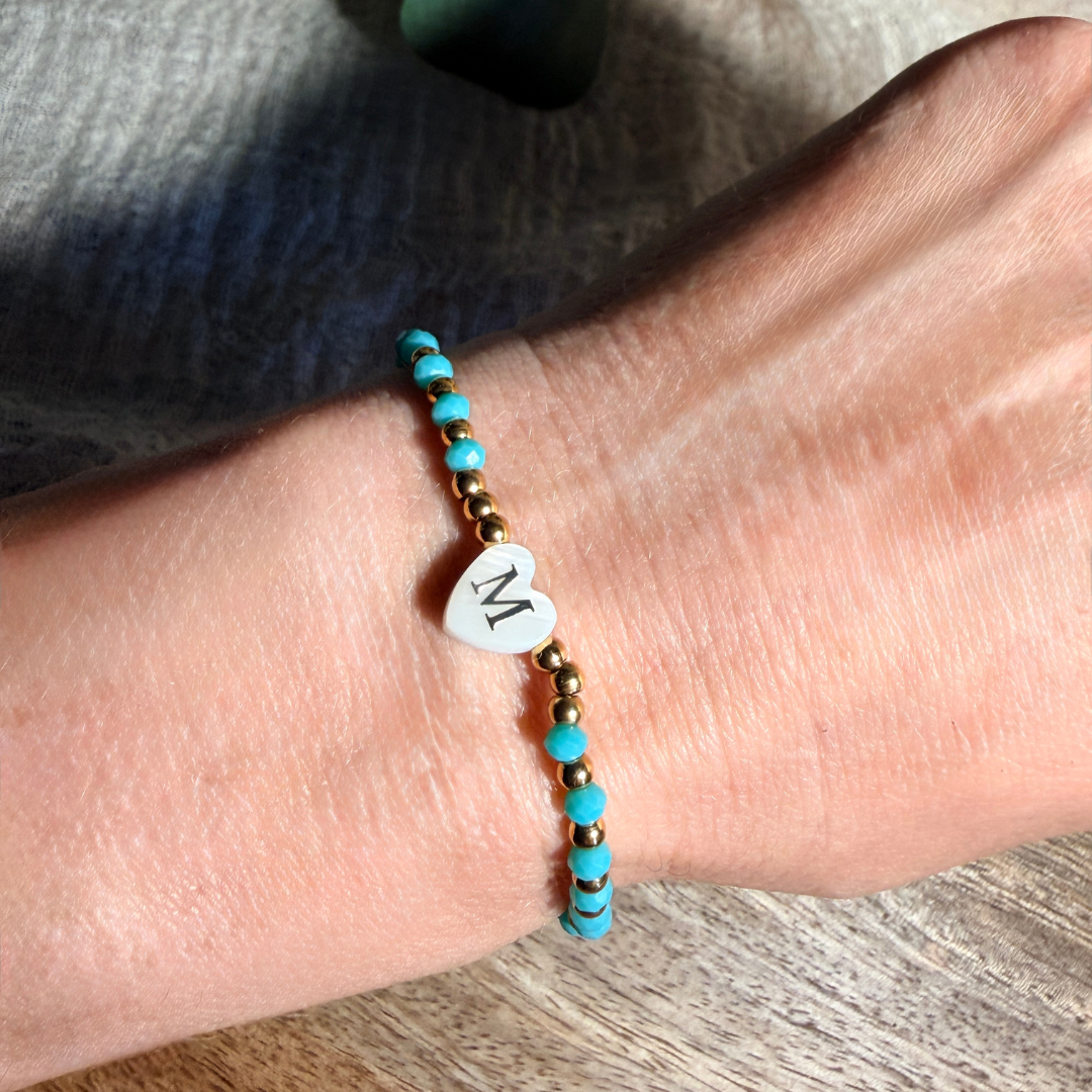 Bracelet femme en perles à facettes de différents coloris, rouge, beige, corail, marine et turquoise, de perles dorées en acier inoxydable et d'un pendentif cœur en véritable nacre de coquillage orné d'une initiale conçu sur mesure avec des perles de trois millimètres fabriquée à la main à Aix-en-Provence